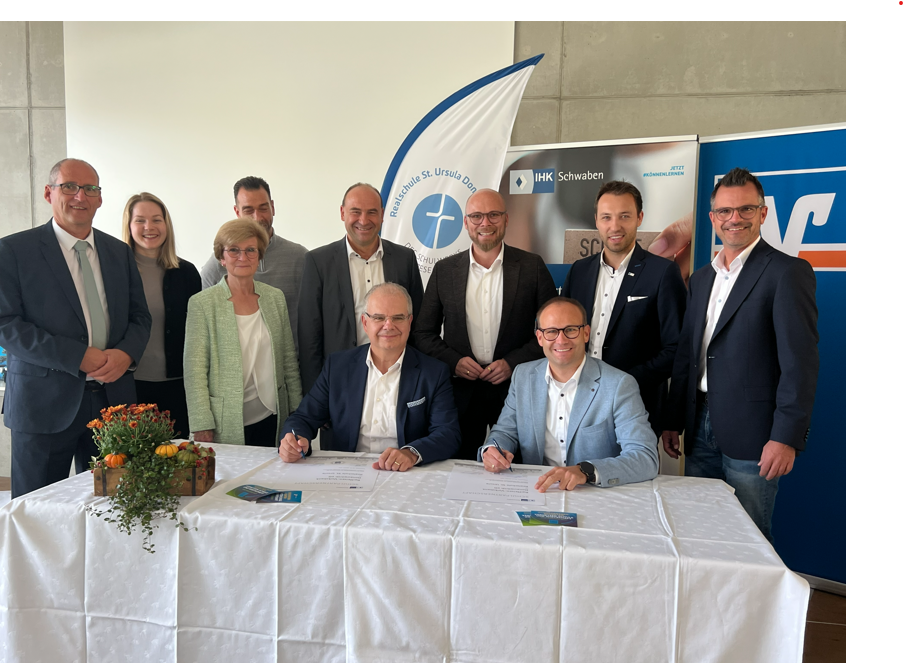 Kooperation zwischen der Raiffeisen-Volksbank Donauwörth eG und der Realschule St. Ursula.  Vorstandssprecher Michael Kruck (sitzend, links) und Schulleiter Tobias Freißler (sitzend, rechts)  unterzeichnen die Verträge im Beisein von Vertretern aus Politik und Wirtschaft.